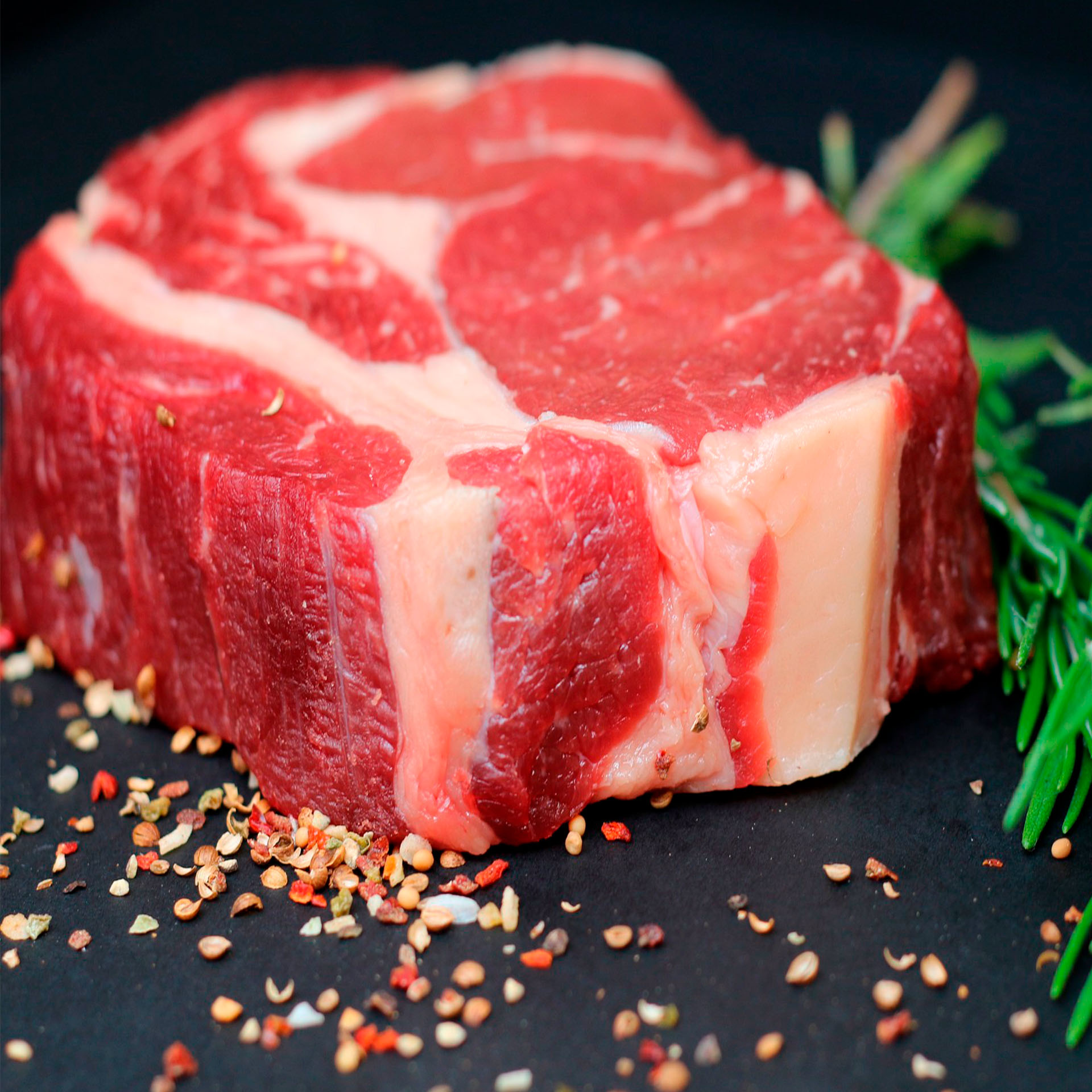trozo de carne, decorado con una rama de tomillo y aliño, sobre un plato negro,